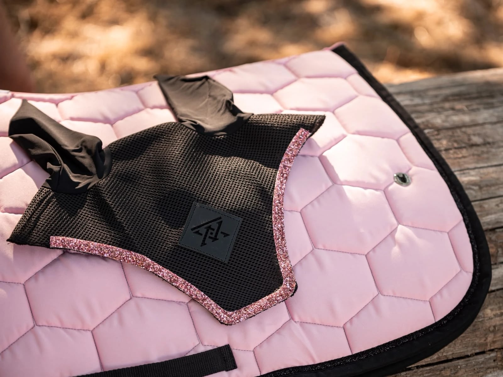 Bonnet noir bordé de paillettes roses posé sur un tapis de selle rose pâle, sur une lisse en bois