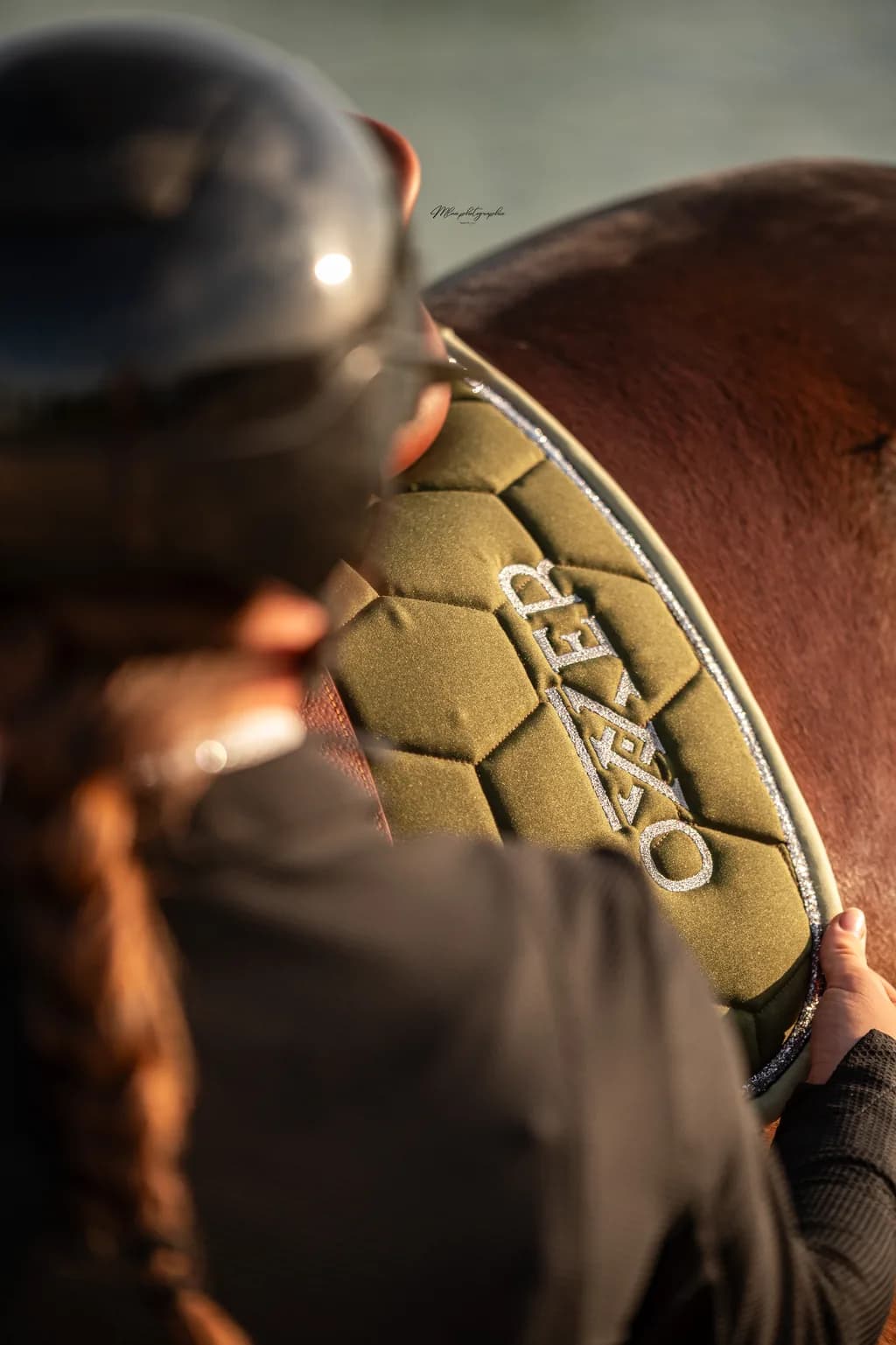 Tapis de selle Oxxer sur un cheval alezan, le logo de la marque sur le flanc